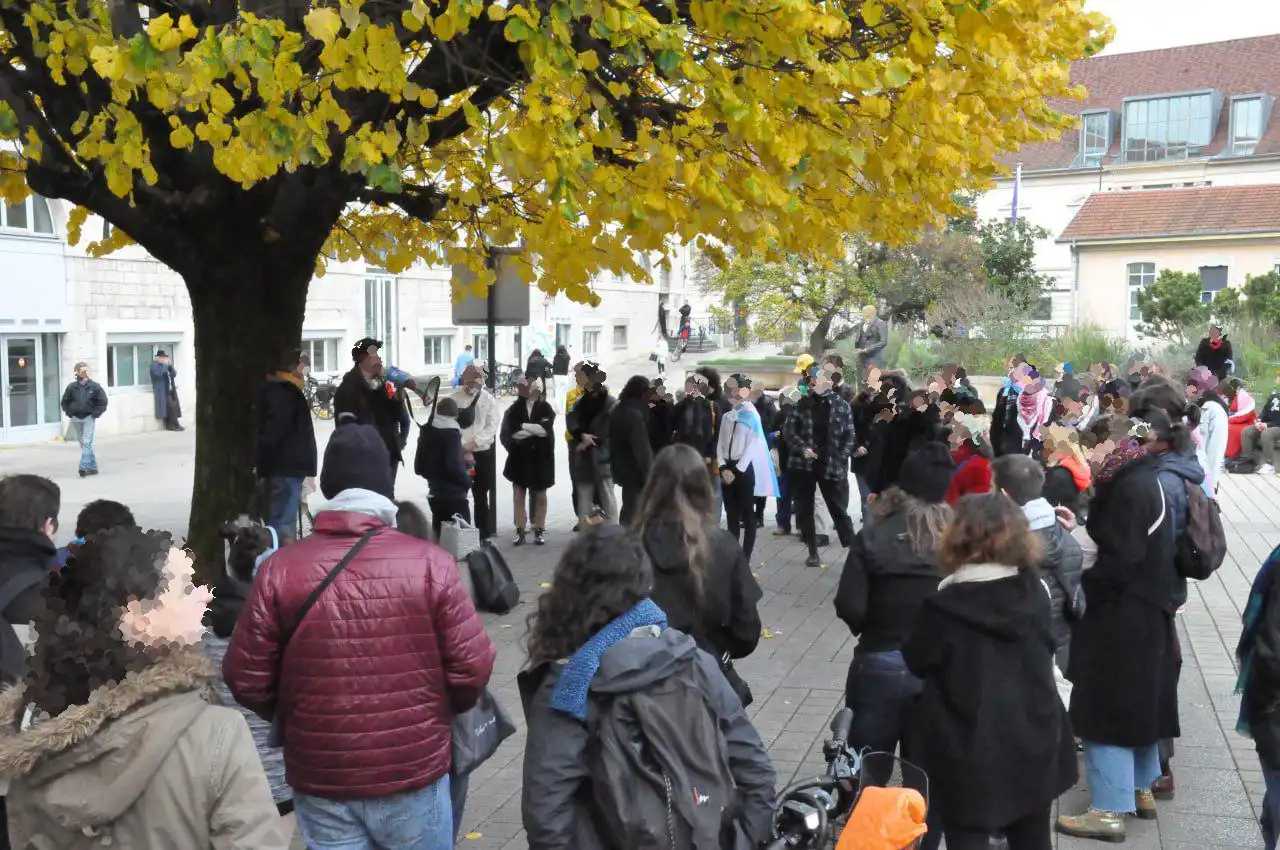 Photo du rassemblement place de l'Esplanade. Un grand nombre de personnes se tiennent debout en arc de cercle autour d'un arbre. Au pied de l'arbre se tiennent deux personnes, une d'entre elles parlant dans un mégaphone.